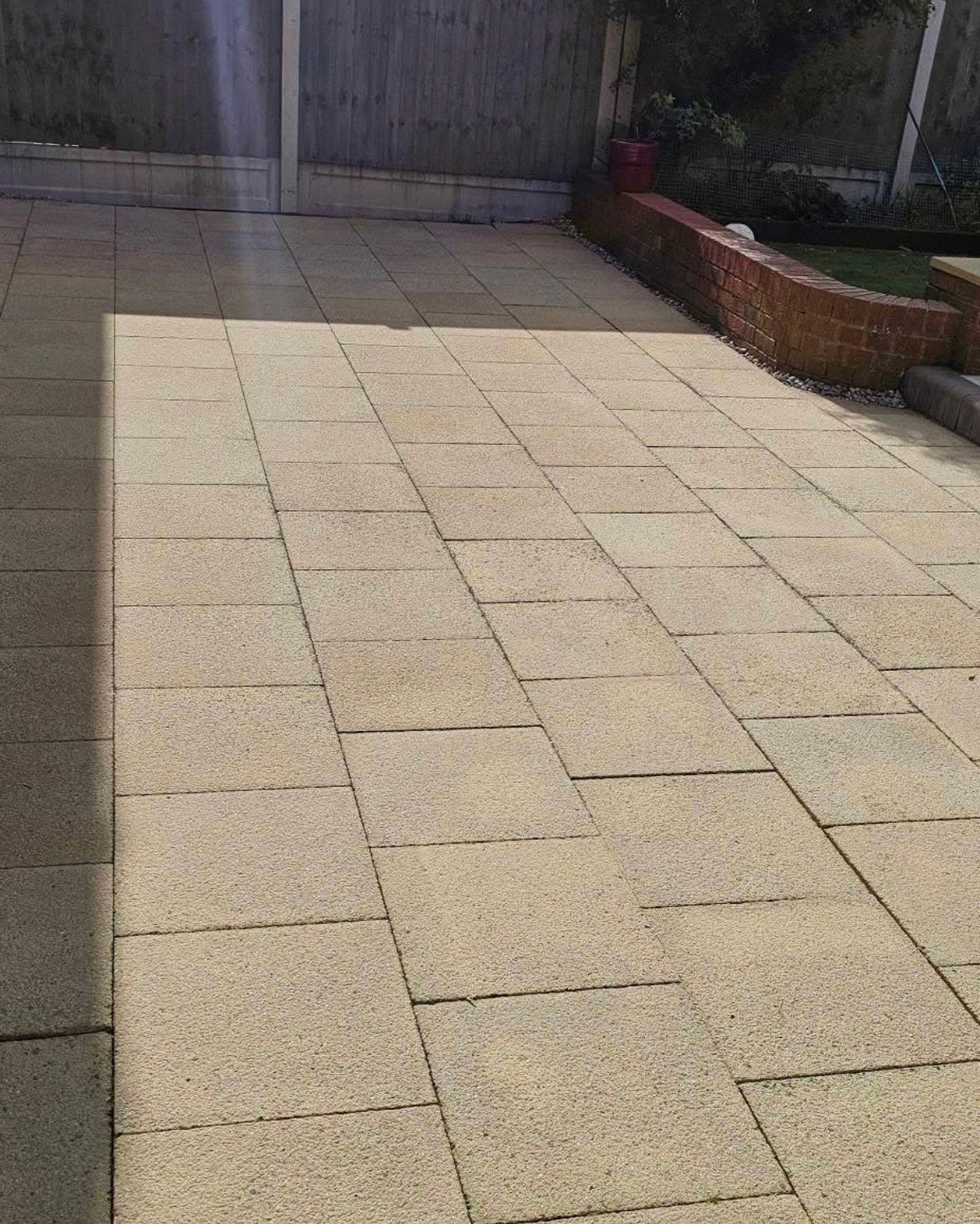 Outdoor patio with beige rectangular pavers in herringbone pattern, bordered by wooden fence and brick planter bed