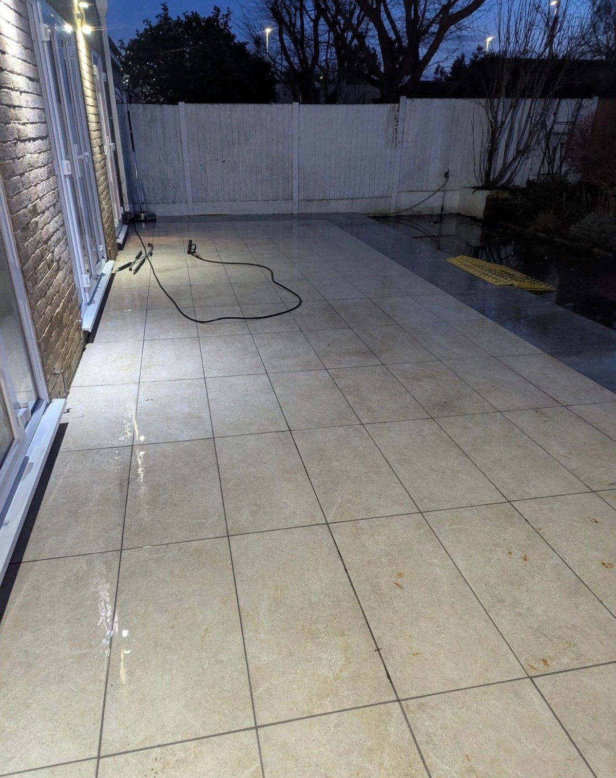 Clean backyard patio with gray tiled flooring and white fence at dusk