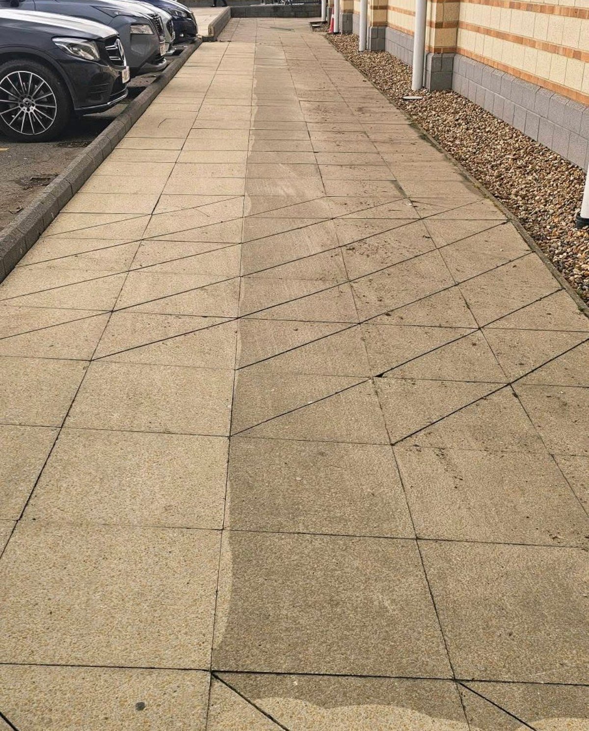 Straight paved walkway with geometric tile pattern before pressure washing
