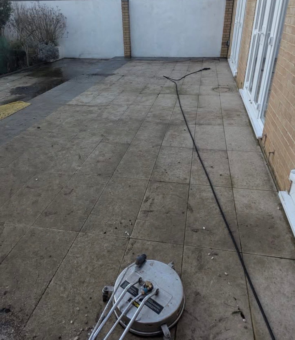 Pressure washer cleaning concrete patio next to brick wall